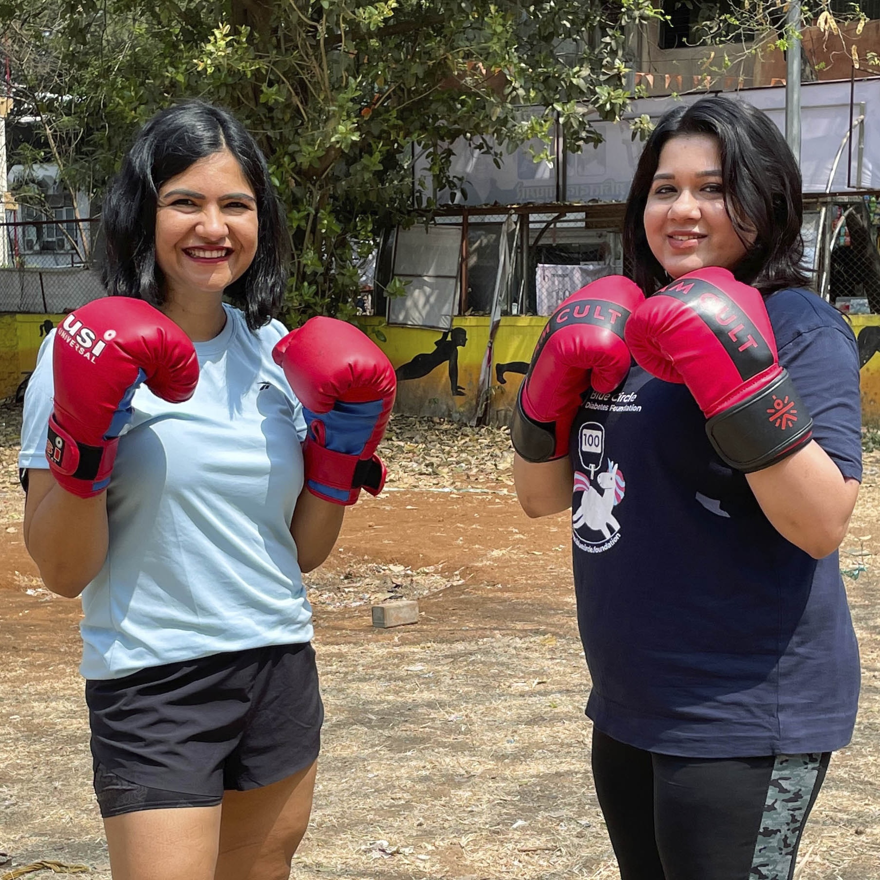 Two women from India wearing boxing gloves and smiling