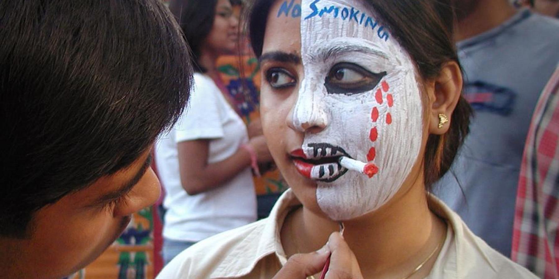 Close up of young woman with cigarette and half of face painted white 