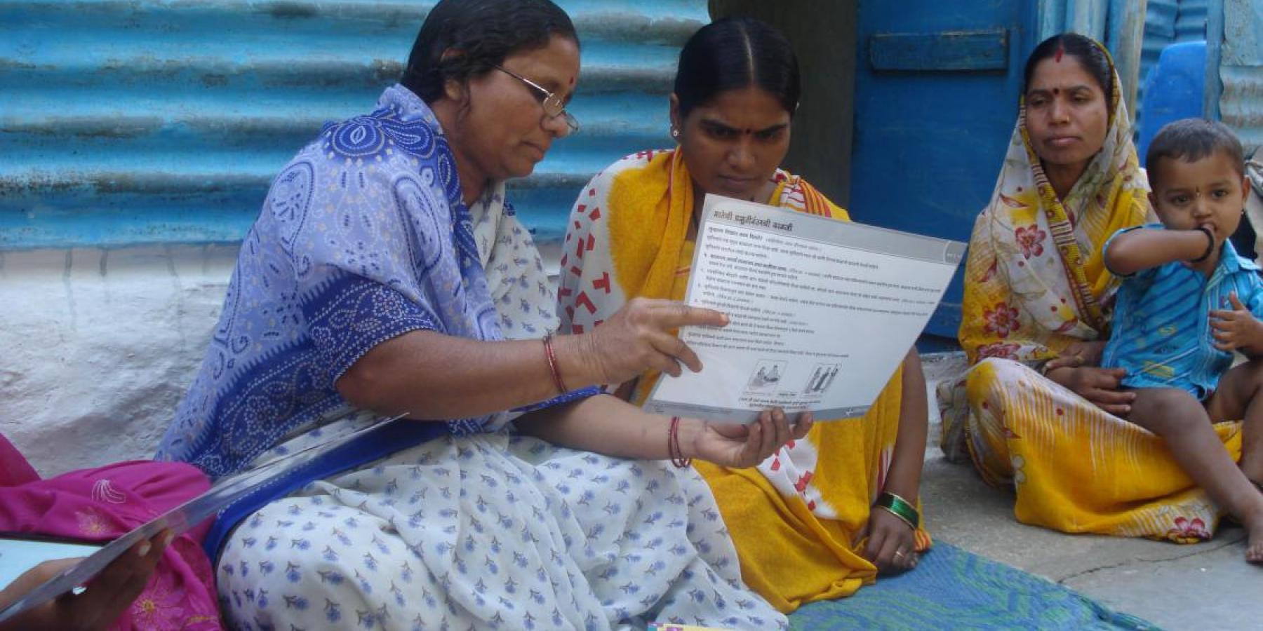 A self-help group (SHG) member provides a mother with information on infant and newborn care during a home visit in India.