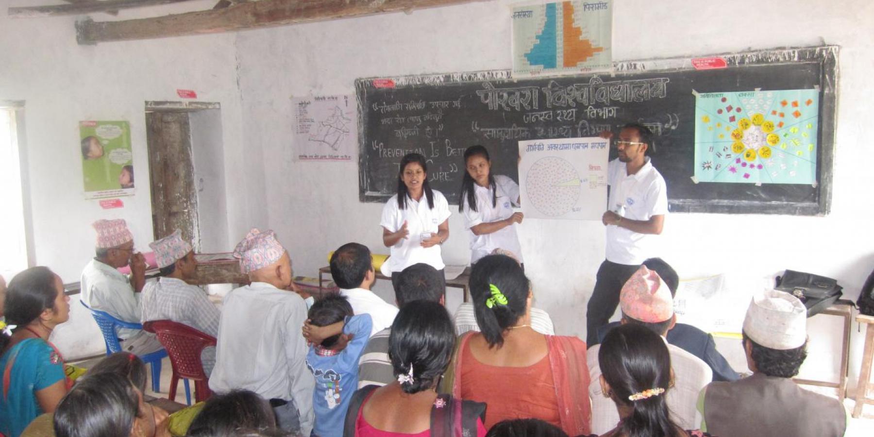 Health volunteers explain a pie chart with data on pregnant women's consumption of tobacco and alcohol to community members in Chidipani, Palpa, Nepal.