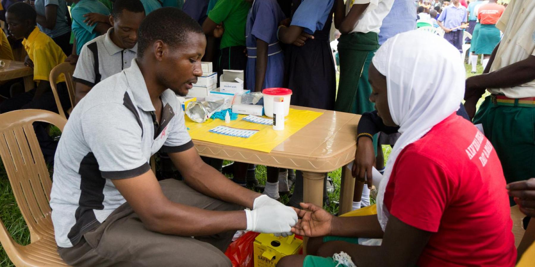  A young man testing a girl for HIV by pricking her finger and drawing blood.