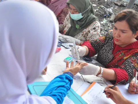 Health worker checking blood sugar levels at a social event in Indonesia
