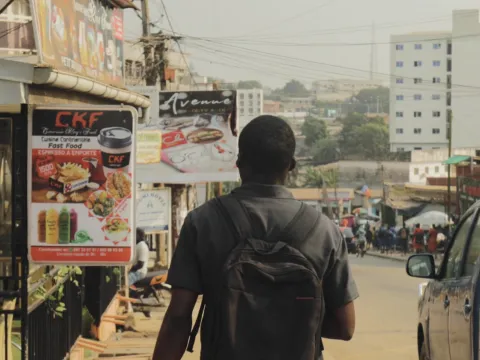 Teenager walks along a street in Yaounde, Cameroon, next to junk food advertisements. Still from 'Africa's diabetes rise' from Turning the Tide series