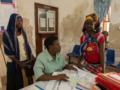 health worker with papers in clinic in Tanzania with two young women