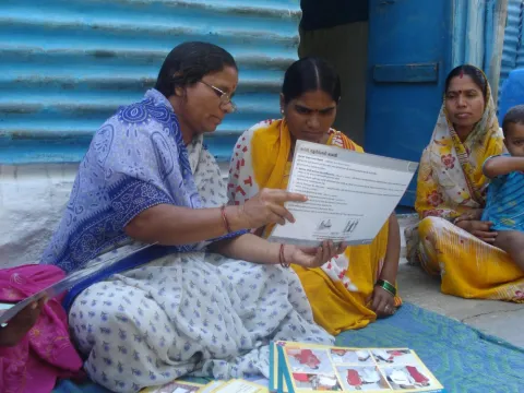 A self-help group (SHG) member provides a mother with information on infant and newborn care during a home visit in India.