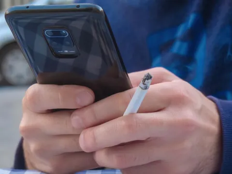A man smoking a cigarette looking at his phone