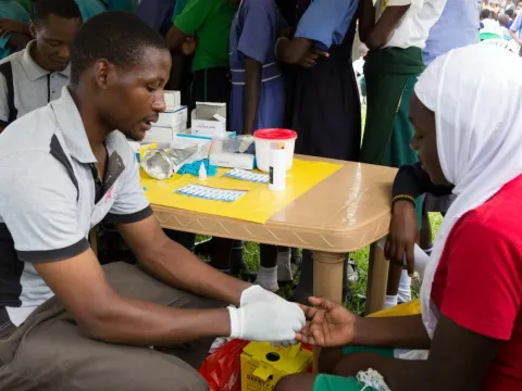  A young man testing a girl for HIV by pricking her finger and drawing blood.