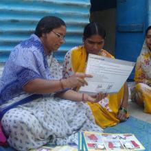 A self-help group (SHG) member provides a mother with information on infant and newborn care during a home visit in India.