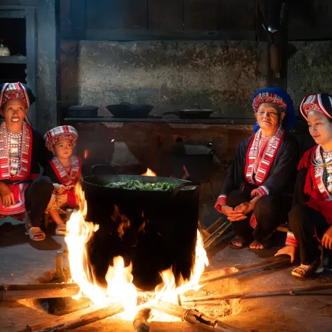 Three women and a child cook on a bonfire inside a house in Vietnam.