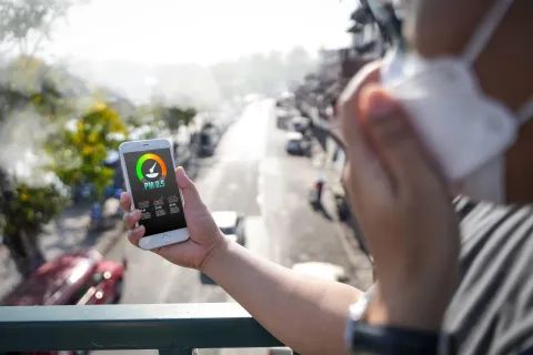 A person checks real-time air pollution levels on their smartphone while wearing a protective mask outdoors