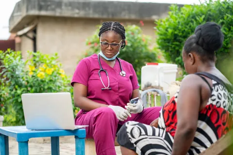 Woman nurse in pink scrubs with patient reviewing info outdoors on computer