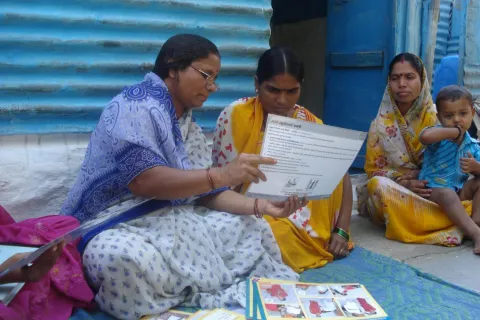A self-help group (SHG) member provides a mother with information on infant and newborn care during a home visit in India.