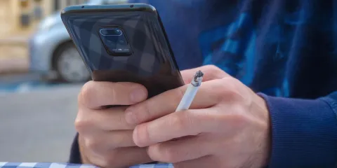 A man smoking a cigarette looking at his phone