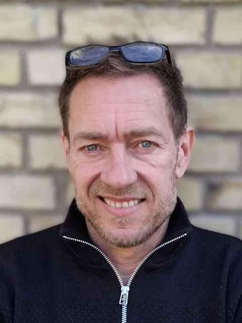 man smiling for portrait in front of brick wall