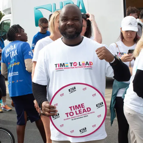 Man holding sign at a community charity event with 'call to lead' for global week for action on ncds
