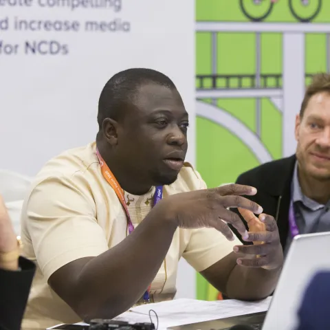NCD Advocate Christ Agbega speaking into a microphone at an event 