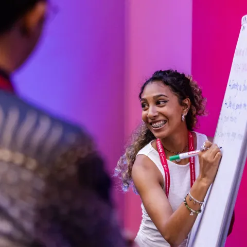 Young woman at Global NCD Alliance Forum 2025 smiling and writing on whiteboard