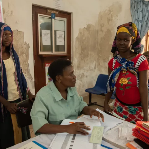 health worker with papers in clinic in Tanzania with two young women